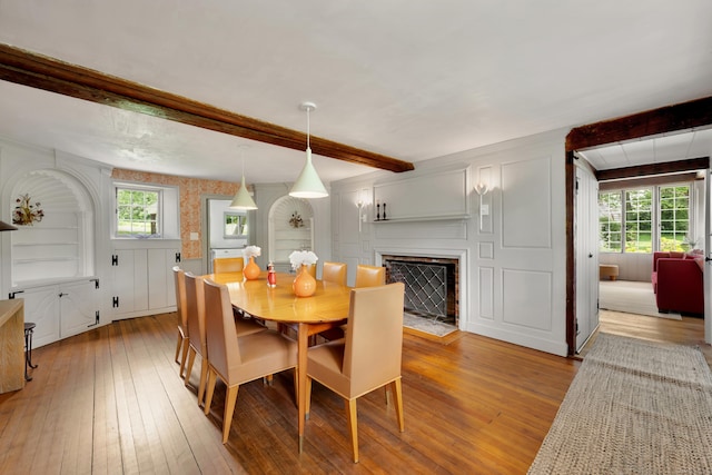 dining space featuring light wood-style floors, beam ceiling, healthy amount of natural light, a fireplace with flush hearth, and a decorative wall
