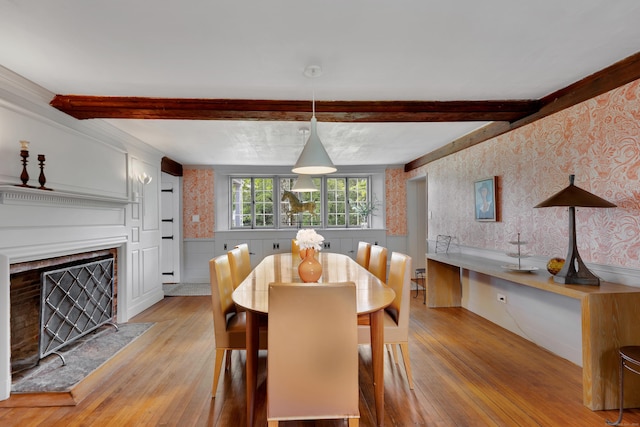 dining room with beam ceiling, light wood-type flooring, a fireplace, and wallpapered walls
