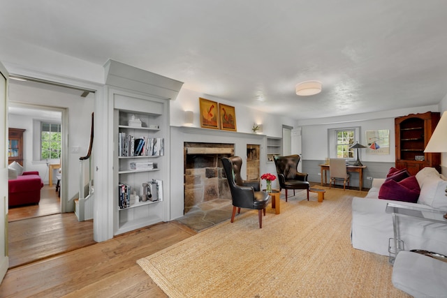 living room featuring wood finished floors, a fireplace with raised hearth, and built in features