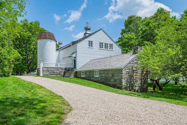 view of home's exterior with stone siding, a lawn, gravel driveway, and a chimney