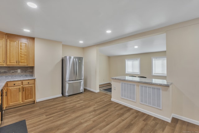 kitchen featuring light stone countertops, backsplash, stainless steel refrigerator, light brown cabinets, and light hardwood / wood-style flooring