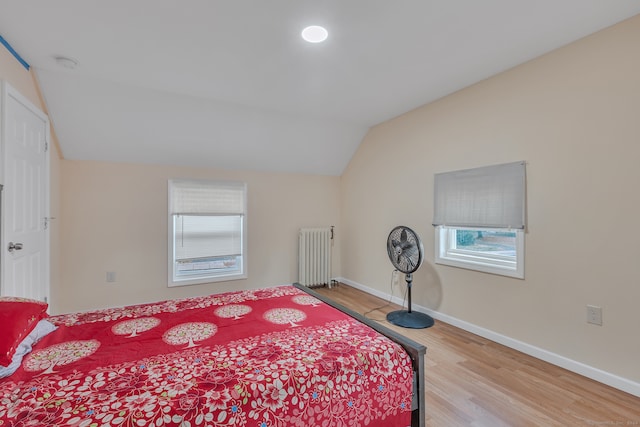 bedroom with radiator, multiple windows, light wood-type flooring, and vaulted ceiling