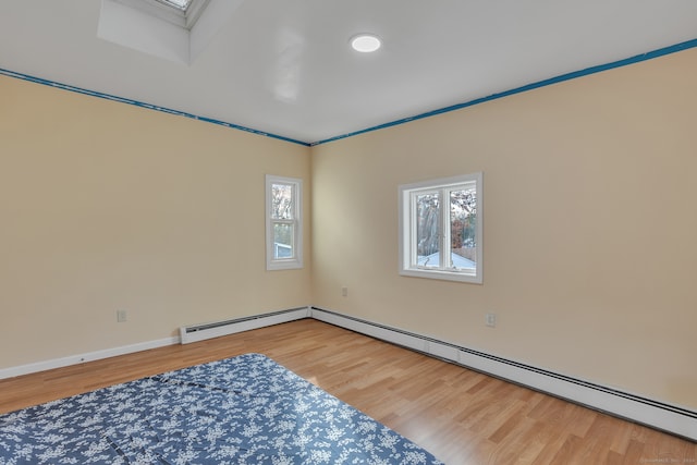 spare room featuring wood-type flooring, a baseboard heating unit, a skylight, and ornamental molding