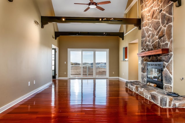 unfurnished living room featuring baseboards, a ceiling fan, wood finished floors, beamed ceiling, and a stone fireplace