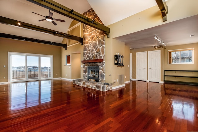 unfurnished living room featuring baseboards, visible vents, wood finished floors, a stone fireplace, and high vaulted ceiling