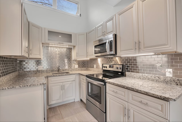 kitchen featuring light stone counters, stainless steel appliances, sink, decorative backsplash, and white cabinets