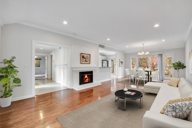 living room with ornamental molding, a chandelier, light hardwood / wood-style floors, and a brick fireplace