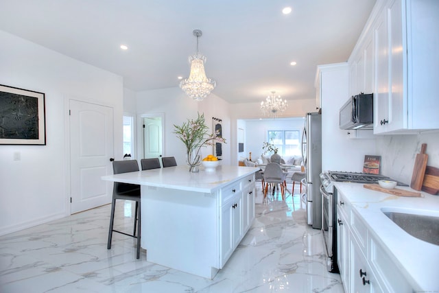 kitchen featuring stainless steel appliances, pendant lighting, a notable chandelier, a center island, and white cabinetry