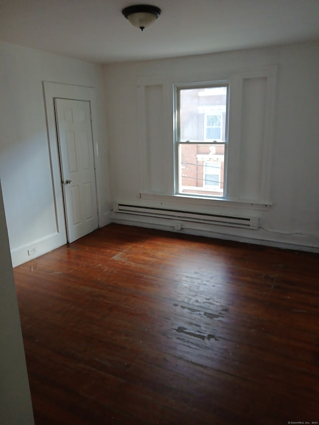 spare room featuring dark wood-type flooring and a baseboard heating unit