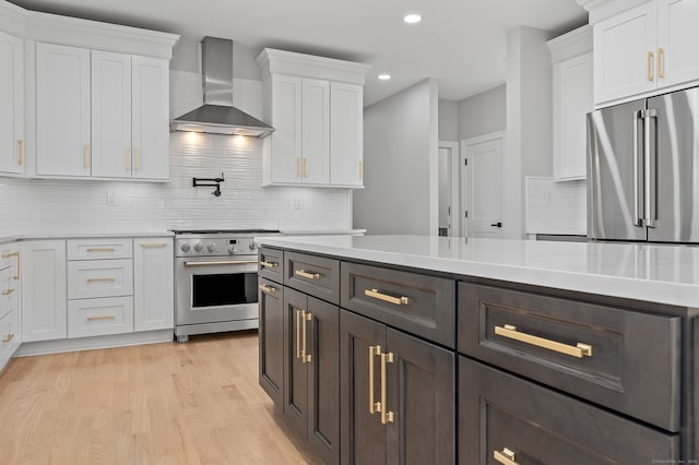 kitchen featuring light wood-type flooring, white cabinetry, high end appliances, and wall chimney range hood