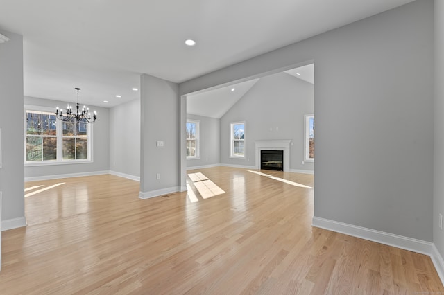 unfurnished living room featuring a chandelier, vaulted ceiling, and light hardwood / wood-style flooring