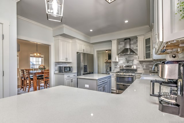 kitchen featuring appliances with stainless steel finishes, ornamental molding, wall chimney exhaust hood, a center island, and hanging light fixtures