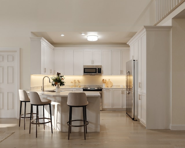 kitchen with a breakfast bar area, light wood-type flooring, white cabinetry, kitchen peninsula, and stainless steel appliances