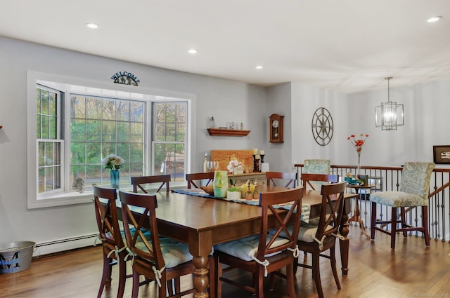 dining space with light hardwood / wood-style flooring, baseboard heating, a healthy amount of sunlight, and a notable chandelier