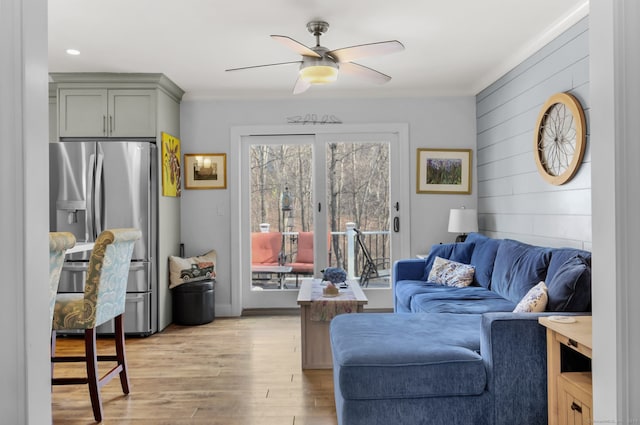 living room with light hardwood / wood-style flooring, ceiling fan, crown molding, and wood walls