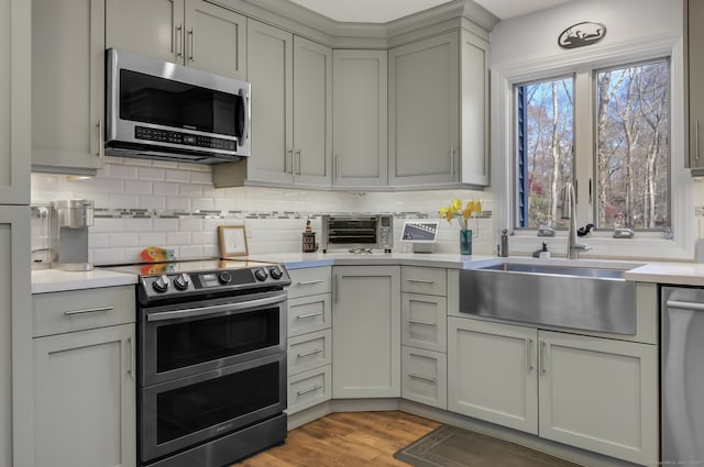 kitchen with backsplash, sink, gray cabinets, appliances with stainless steel finishes, and light hardwood / wood-style floors