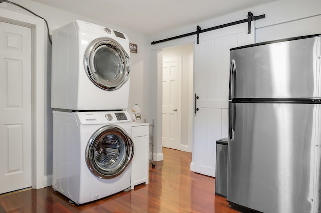 clothes washing area featuring a barn door, dark hardwood / wood-style flooring, and stacked washer and dryer