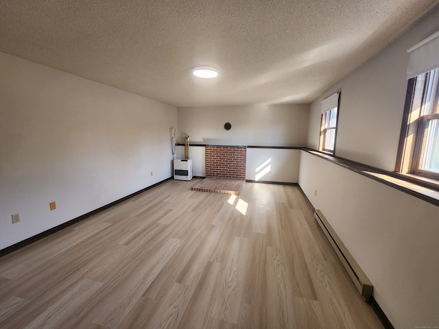 spare room with light wood-type flooring, a textured ceiling, and a baseboard heating unit