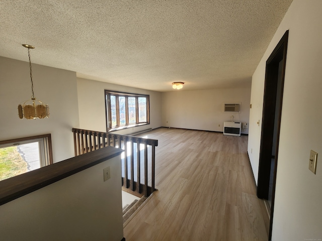 hall with light hardwood / wood-style floors, a wall mounted air conditioner, a textured ceiling, heating unit, and an inviting chandelier