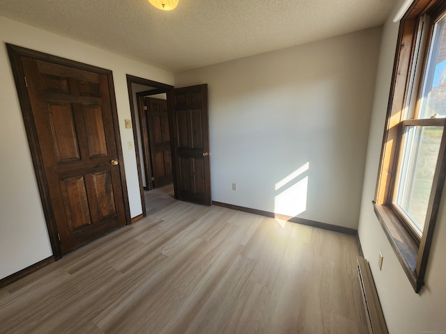 unfurnished bedroom featuring light wood-type flooring, a baseboard radiator, and a textured ceiling