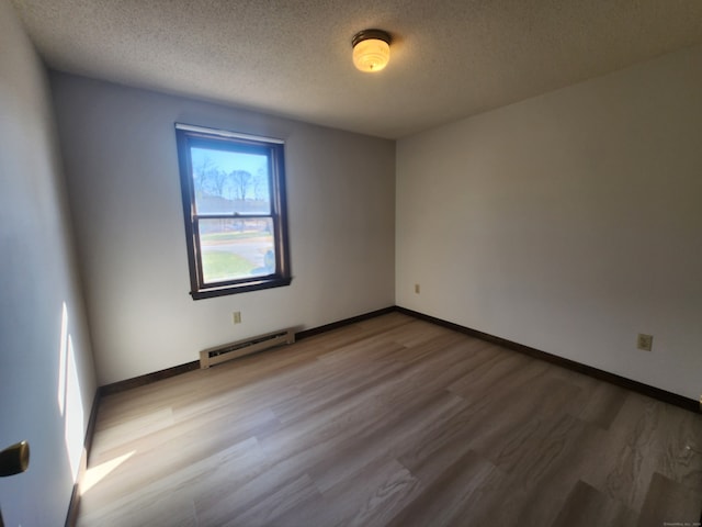 empty room featuring hardwood / wood-style flooring, baseboard heating, and a textured ceiling