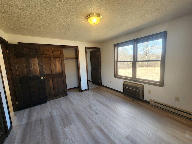 unfurnished bedroom with a baseboard heating unit, an AC wall unit, light hardwood / wood-style flooring, and a textured ceiling