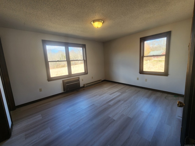 empty room featuring light hardwood / wood-style floors, baseboard heating, a textured ceiling, and a wall mounted air conditioner