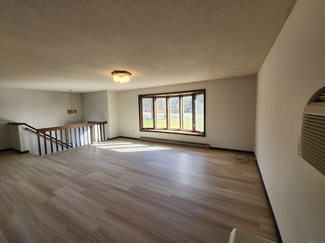 empty room with light hardwood / wood-style floors, a textured ceiling, and a baseboard heating unit