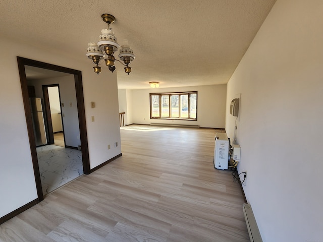 unfurnished room with a textured ceiling, a notable chandelier, light hardwood / wood-style floors, and a baseboard heating unit