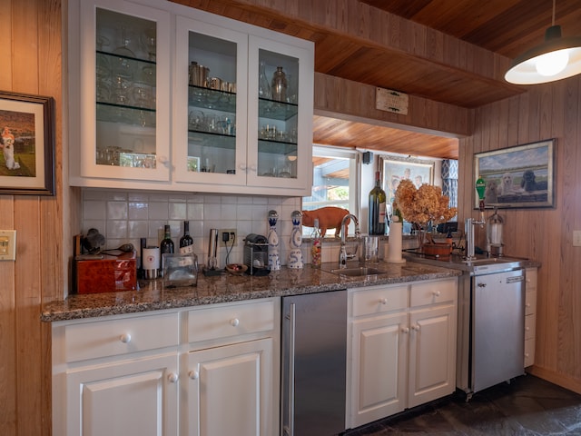 kitchen featuring dishwasher, white cabinetry, wooden walls, and sink