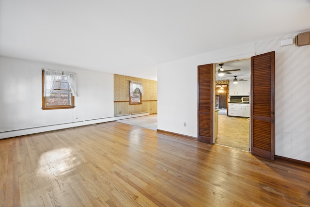 interior space with baseboard heating, ceiling fan, and light hardwood / wood-style flooring