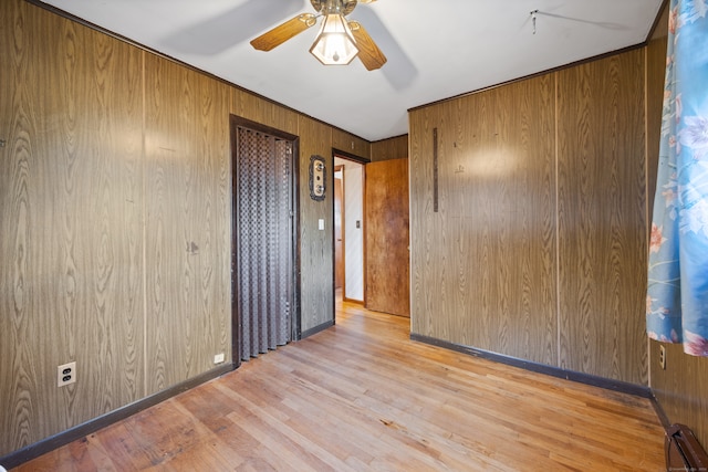 unfurnished room featuring light wood-type flooring, wooden walls, ceiling fan, and a baseboard radiator