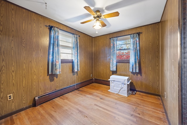 unfurnished room with wood walls, wood-type flooring, ceiling fan, and a baseboard heating unit