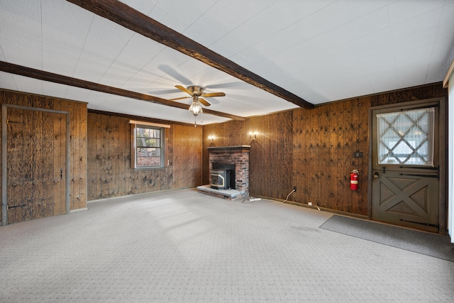 unfurnished living room featuring beamed ceiling, wooden walls, a wood stove, and ceiling fan