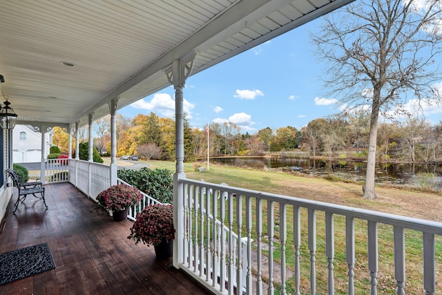 wooden terrace with a porch, a water view, and a lawn