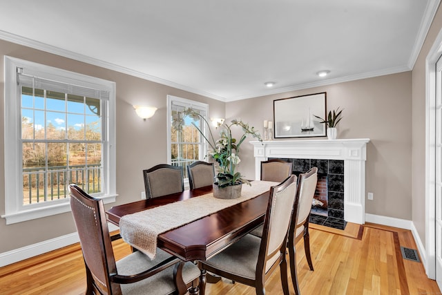 dining area with light wood-type flooring, ornamental molding, and a tiled fireplace