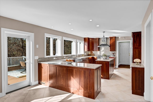 kitchen with decorative light fixtures, plenty of natural light, wall chimney range hood, and kitchen peninsula