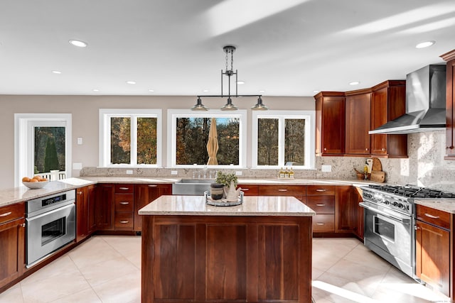 kitchen with a center island, hanging light fixtures, wall chimney exhaust hood, light stone countertops, and appliances with stainless steel finishes