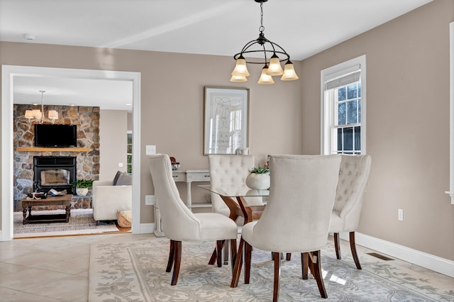 dining space featuring tile patterned floors, a stone fireplace, and an inviting chandelier