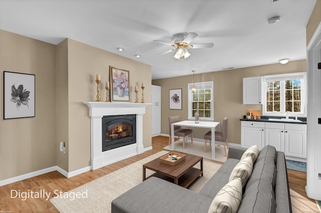 living room with light wood-type flooring, ceiling fan, and sink