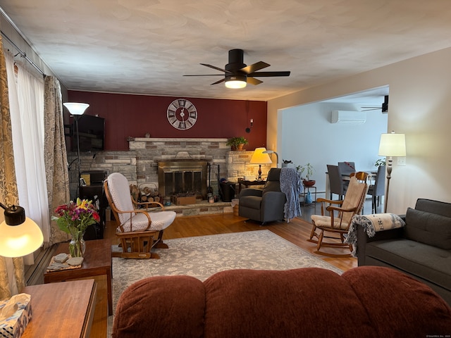 living room with a fireplace, a wall unit AC, wood-type flooring, and ceiling fan