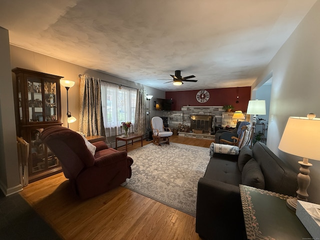 living room featuring a stone fireplace, hardwood / wood-style floors, and ceiling fan