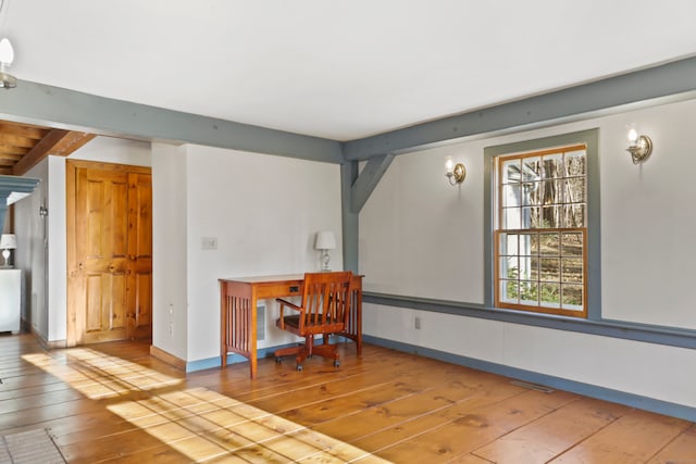 empty room featuring light wood-type flooring and beam ceiling