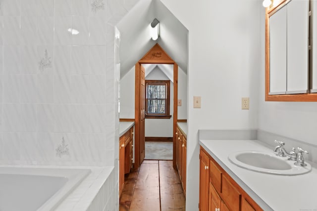 bathroom with tiled bath, vanity, vaulted ceiling, and wood-type flooring