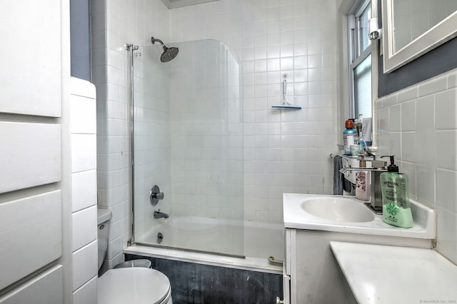 full bathroom with tiled shower / bath, backsplash, vanity, toilet, and tile walls