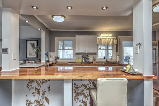 kitchen with sink, a breakfast bar, ornamental molding, white cabinets, and wood counters