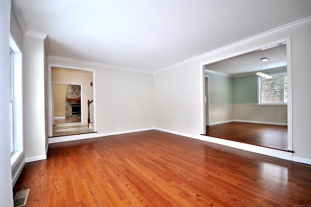 empty room featuring hardwood / wood-style flooring, ornamental molding, and a stone fireplace