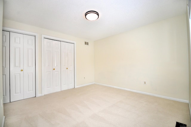 unfurnished bedroom featuring multiple closets and light carpet