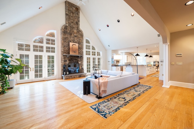 living room featuring a fireplace, light hardwood / wood-style floors, high vaulted ceiling, and decorative columns