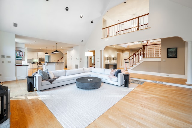 living room with ornate columns, light wood-type flooring, and high vaulted ceiling